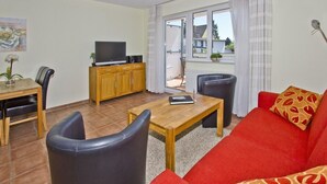 Un salon avec un canapé rouge, une table basse en bois, un téléviseur posé sur un meuble en bois, et un coin repas avec des chaises et une table.