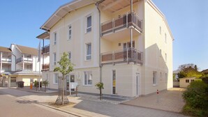 Un immeuble résidentiel à plusieurs étages, doté de balcons, avec un petit arbre devant et un ciel dégagé.