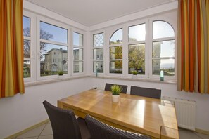 Un comedor con una mesa de madera, seis sillas y ventanas grandes con cortinas.
