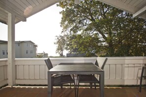 A covered patio with a table and chairs, surrounded by a white fence, overlooking a residential area with houses and trees. - Apartment with a view of the sea, access to the pool and sauna - Haus Blick zur See FeWo 15 - (Göhren)