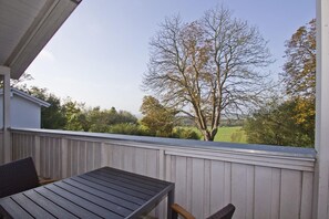 Eine Holzterrasse mit Tisch und Stühlen, mit Blick auf einen Baum und eine grüne Landschaft.