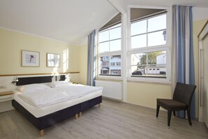 A hotel room with a bed, a chair, a nightstand, and a window with curtains. - Apartment with balcony, use of swimming pool and sauna - Haus Blick zur See Apartment 14 - (Göhren)