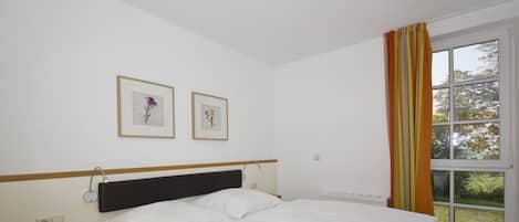 A bedroom with a bed, bedside table, nightstand, and a window with curtains.