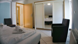 Une chambre d’hôtel avec un lit, une chaise, une armoire et une salle de bain visible à travers une porte ouverte.