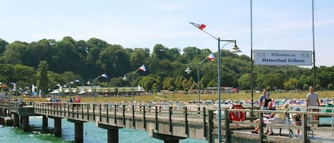 En brygga med en skylt som välkomnar besökare till badorten Ostseebad Göhren, med utsikt över vattnet och ett skogsområde i bakgrunden.