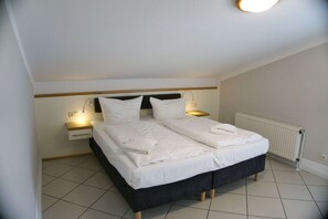 A neatly made twin bed with white linens, a bedside table with a lamp, and a radiator on the wall. - Apartment with a view of the sea, access to the pool and sauna - Haus Blick zur See FeWo 10 - (Göhren)