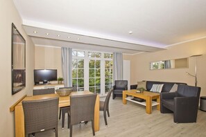 A modern living room with a dining area, a sofa, a TV, and large windows.