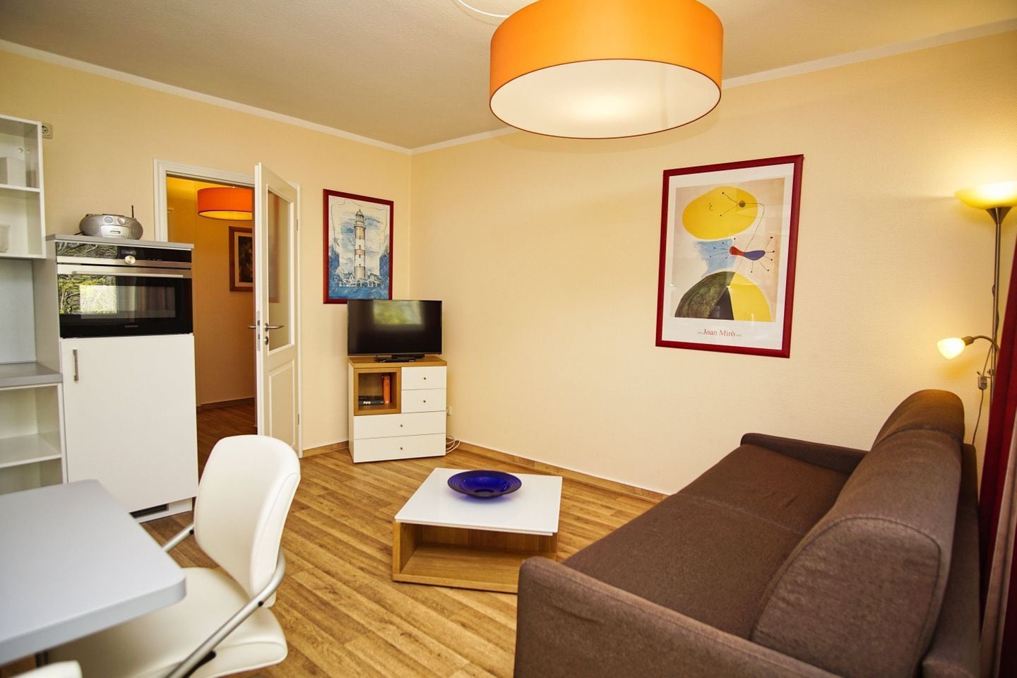 A compact living space with a kitchenette, a dining area, a sofa, and artwork on the walls.