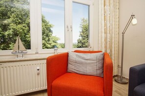 A room with a large window, a radiator, a small sailboat model, a striped pillow, and a floor lamp.