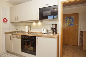 A compact kitchen with white cabinets, a stove, a microwave, a coffee maker, and a map on the wall.