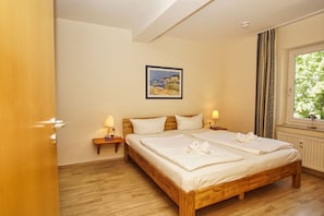 A hotel room with a wooden bed, two bedside tables with lamps, a framed picture on the wall, and a window with curtains. - Close to the beach, sauna + swimming pool free of charge - Strandresidenz Brandenburg FeWo 31 - House (Göhren)