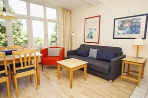 Un salon avec un canapé, une petite table, un fauteuil, une lampe et des œuvres d’art accrochées au mur.