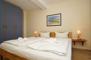 A hotel room with a double bed, two bedside tables with lamps, a wardrobe, and a painting on the wall.