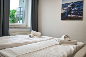 A hotel room with two beds, a window with curtains, and a painting of a rocky coastline. - Close to the beach, balcony, AHOI adventure pool free of charge - Strandresidenz Brandenburg FeWo 36 (Göhren)