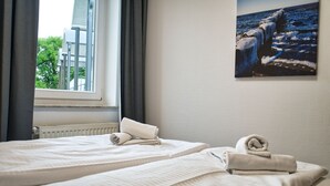 Een hotelkamer met twee bedden, een raam met gordijnen, en een schilderij van een rotsachtige kustlijn.