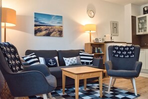 A cozy living room with a sofa, two armchairs, a coffee table, and a bookshelf. - Close to the beach, balcony, free AHOI adventure pool - Strandresidenz Brandenburg FeWo 36 (Göhren)