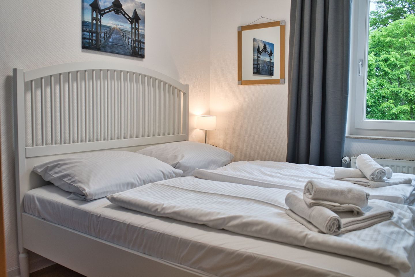 A hotel room with two beds, a headboard, a window with curtains, and two framed pictures on the wall.