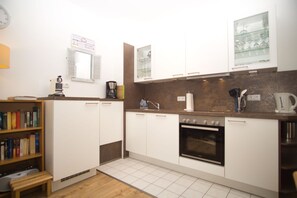 A modern kitchen with white cabinets, a built-in oven, a coffee maker, and a bookshelf.