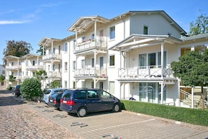 A row of white multi-story buildings with balconies, parked cars, and a paved walkway. - Close to the beach, balcony, free AHOI adventure pool - Strandresidenz Brandenburg FeWo 04 (Göhren)