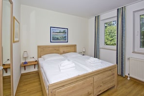 A neatly made bed in a room with a wooden headboard, a bedside table with a lamp, a framed picture on the wall, and a window with curtains. - Close to the beach, balcony, free AHOI adventure pool - Strandresidenz Brandenburg FeWo 04 (Göhren)