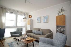 A modern living room with a sofa, two armchairs, a coffee table, and a wooden cabinet. - Central apartment with a terrace, access to the pool and sauna - Villa Anni FeWo 02 - (Göhren)