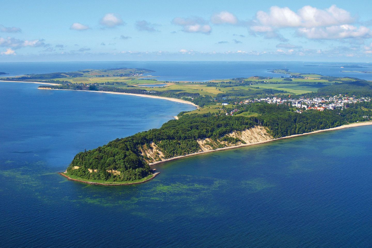 Eine Luftaufnahme einer Küstenlandschaft mit einer kleinen Insel, einem Strand und einer Stadt in der Ferne.