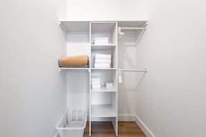 Un armario blanco con estantes y espacio para colgar, una toalla color beige y un cesto de ropa blanca.