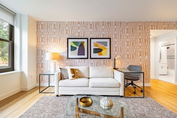 A modern living room with a white sofa, a glass coffee table, and abstract art on the wall.