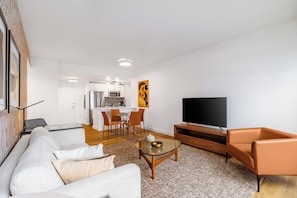 Una sala de estar moderna con sofá, mesa de centro y televisor. En el fondo, un área de comedor con sillas y una mesa.