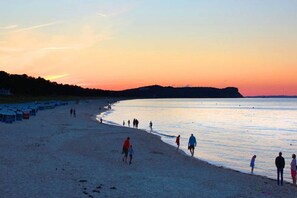 A beach with people walking along the shore, a clear sky, and a distant landmass. - Die Wohnung 05 in der Residenz Strandeck im Ostseebad Göhren - Residenz Strandeck (Göhren)