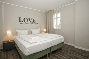 A neatly made double bed with white linens, two bedside lamps, a suitcase, and a wall with a motivational quote. - Die Wohnung 05 in der Residenz Strandeck im Ostseebad Göhren - Residenz Strandeck (Göhren)