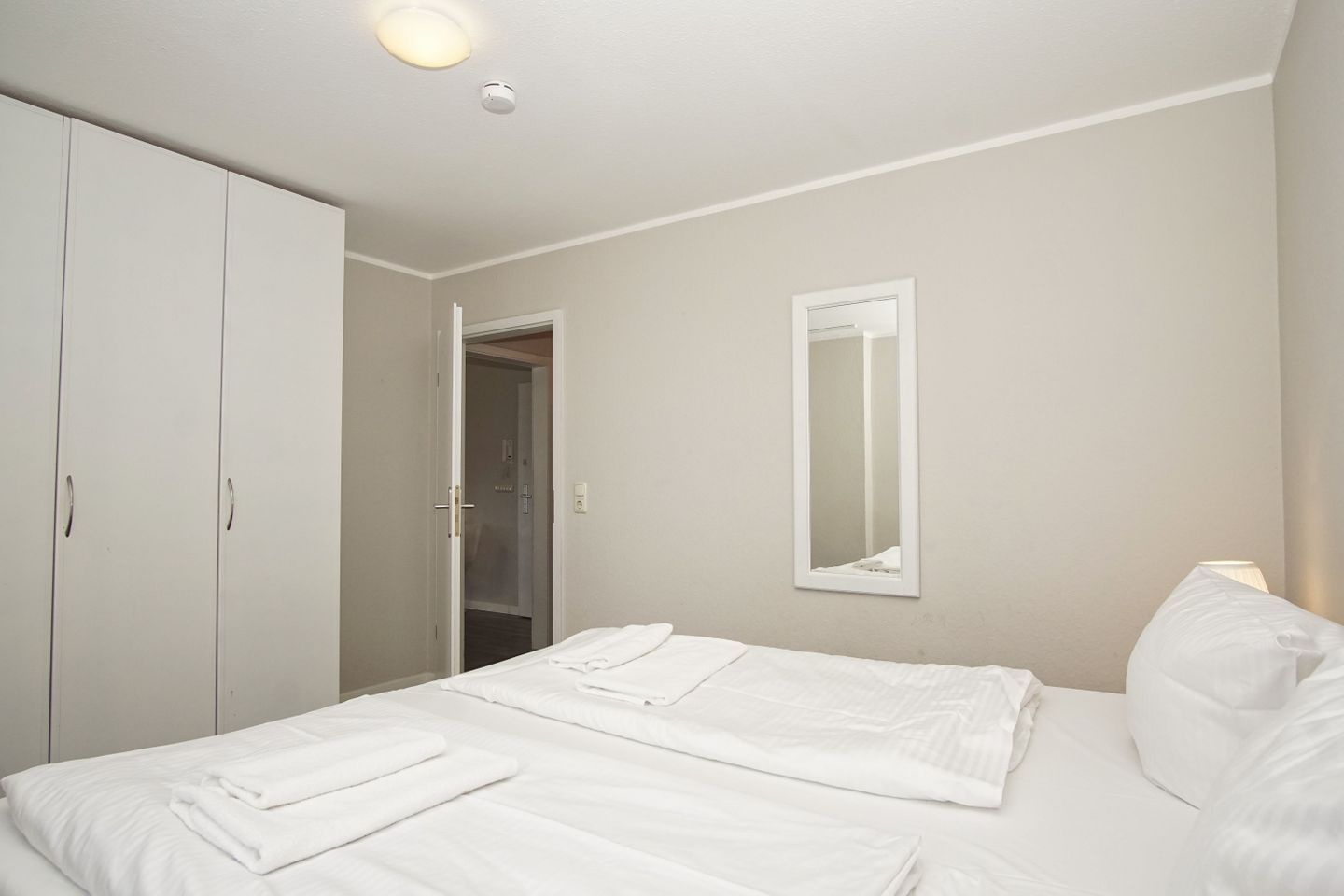 A bedroom with a bed, a wardrobe, a mirror, and a door leading to a bathroom.