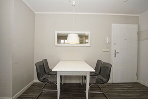 A small, modern room with a white table and two chairs, a hanging light fixture, and a door with a lock. - Die Wohnung 05 in der Residenz Strandeck im Ostseebad Göhren - Residenz Strandeck (Göhren)