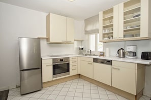 A modern kitchen with a stainless steel refrigerator, a built-in oven, a dishwasher, and a coffee maker.