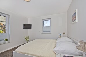 A bedroom with a bed, a TV, a window, and a small table with a lamp. - Cozy vacation apartment with terrace and garden - Ferienhaus Zaunkönig FeWo EG (Gager)