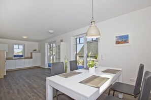 A modern kitchen with white cabinets, a dining area with a white table and chairs, and a large window with a view of the outdoors. - Cozy vacation apartment with terrace and garden - Ferienhaus Zaunkönig FeWo EG (Gager)