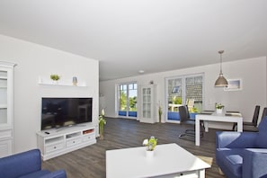 A modern living room with a flat-screen TV, white furniture, and a dining area with a table and chairs.
