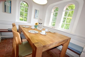 Een eetgedeelte met een houten tafel voor vier personen, omgeven door witte muren en grote, gebogen ramen.