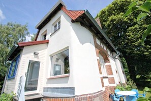 Een tweelaags huis met een witte gevel en een rood dak. Er is een groot raam op de tweede verdieping en een deur op de begane grond.