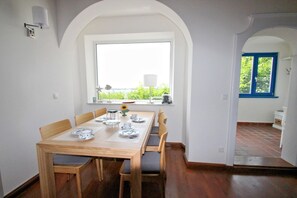 A dining area with a wooden table set for four, a window with a view, and a door leading to another room.
