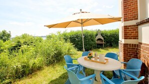 Eine Terrasse im Freien mit einem runden Tisch, blauen Stühlen, einem Sonnenschirm und einer Backsteinmauer.