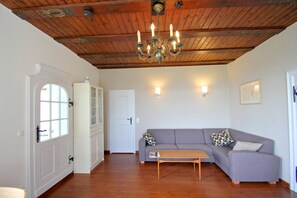 A room with a wooden ceiling, a grey sofa, a wooden table, a white cabinet, and two wall-mounted lights. - Villa Hermine - a fabulous villa in an idyllic location with a view of the sea - Villa (Altefähr)