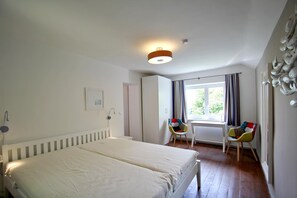 A bedroom with two beds, a window with curtains, a radiator, and a chair with colorful cushions. - Villa Hermine - fabulous villa in an idyllic location with sea views - Villa (Altefähr)