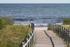 A wooden boardwalk leading to a beach with a person in the distance. - Villa Hermine - fabulous villa in an idyllic location with sea views - Villa (Altefähr)