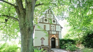 Eine Kirche mit Ziegelverkleidung, Bogenfenstern und einem Glockenturm, umgeben von üppigem Grün.
