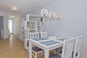 Een eetgedeelte met een witte tafel en stoelen, een wit dressoir met decoratieve objecten, en drie hangende hanglampen.
