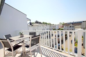 Ein Balkon mit Tisch und Stühlen, einem Blumentopf und einem weißen Zaun.