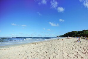 Ein weiter Sandstrand mit Fußabdrücken, Zelten und Menschen.