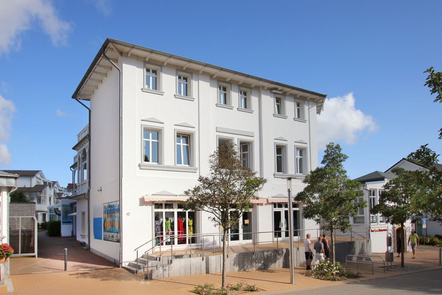 A multi-story white building with a central entrance, a staircase, and a small outdoor seating area.