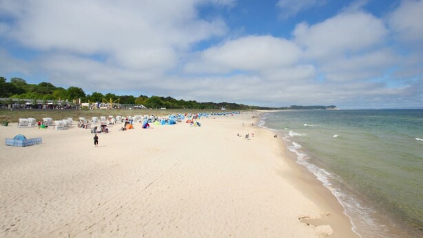 Une vaste plage de sable fin, parsemée de tentes et fréquentée par des baigneurs, un ciel dégagé et une mer calme.